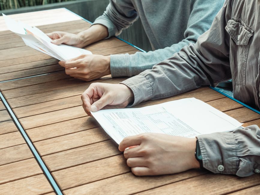 Two people reviewing business documents at an outdoor table, focused on paperwork.