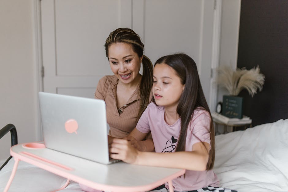 Asian woman and young girl learning on a laptop at home, engaged in online education.
